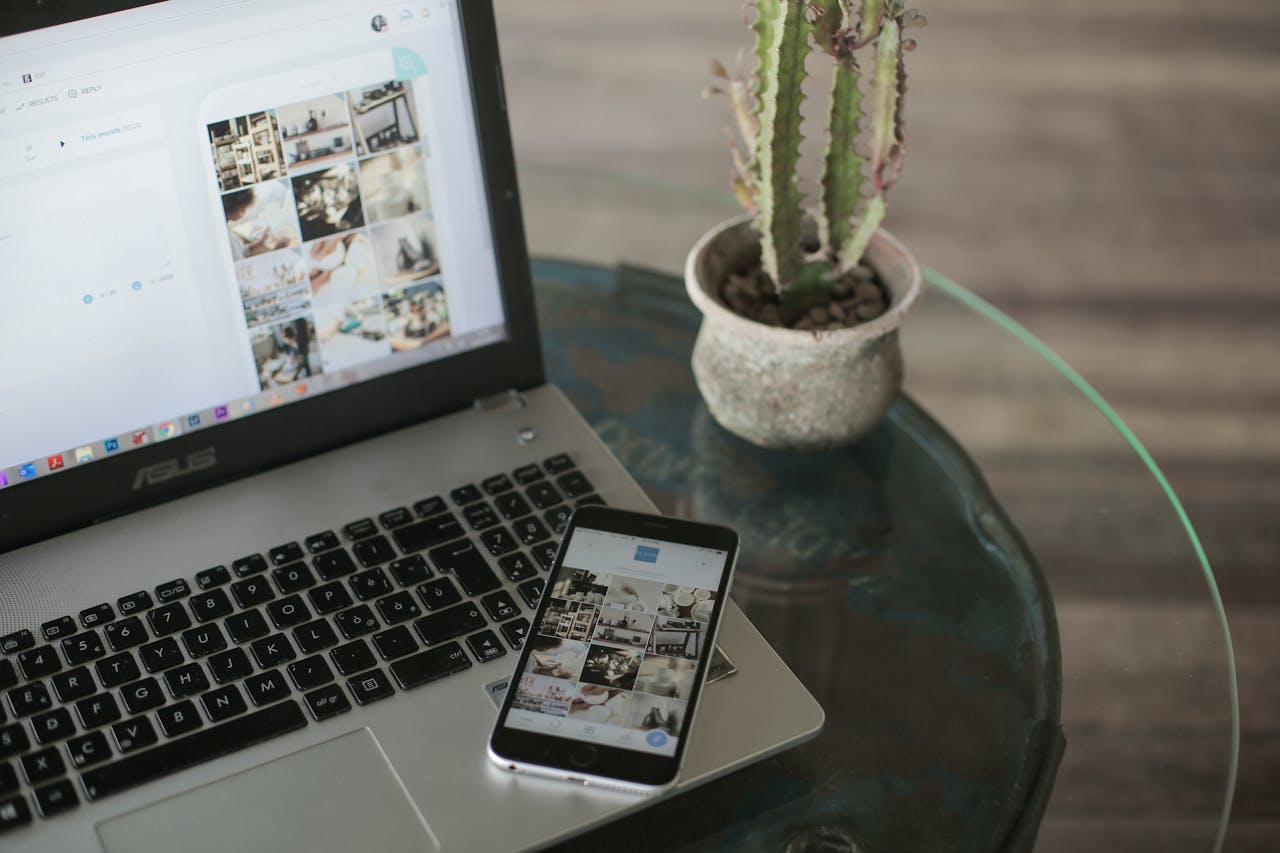 A laptop and smartphone displaying social media apps next to a cactus on a glass table.